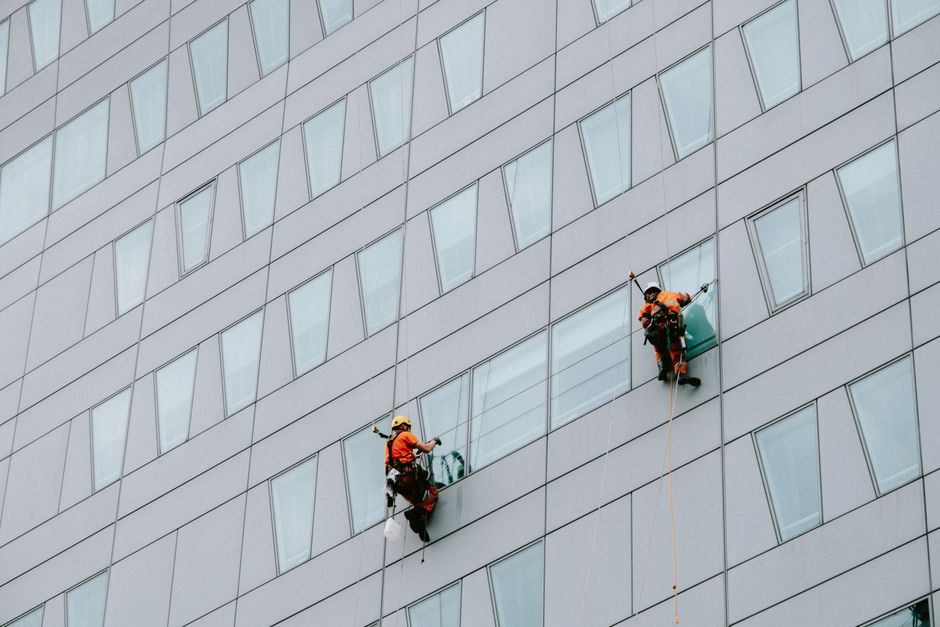 High-rise window washers in safety gear cleaning a skyscraper facade.