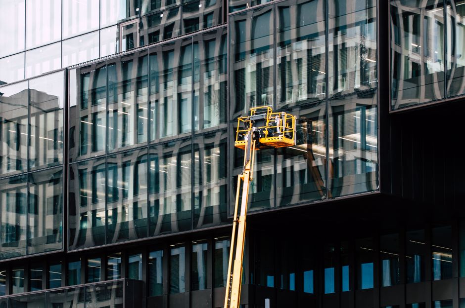 Workers on a lift cleaning windows of a modern glass building exterior.